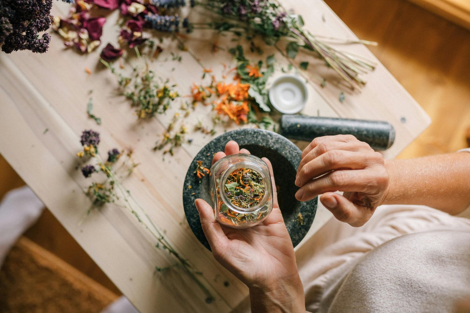 Home Top view of hands preparing herbs and dried flowers using a mortar and pestle on a wooden table.